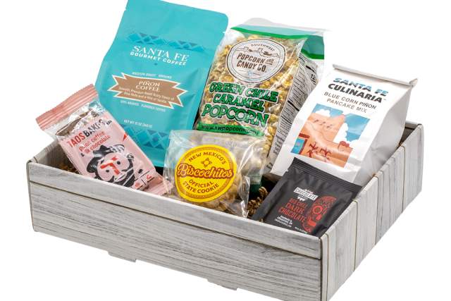 Assorted gourmet snacks including Santa Fe popcorn, biscochitos, and other packaged treats in a wooden gift box.
