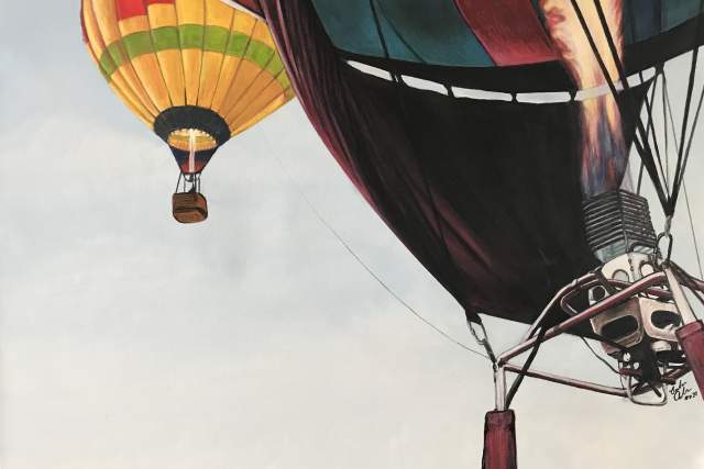 A vibrant painting of two hot air balloons in flight. One balloon is in the foreground with a colorful pattern and a visible burner flame, while another smaller balloon with a yellow and green pattern floats in the background.