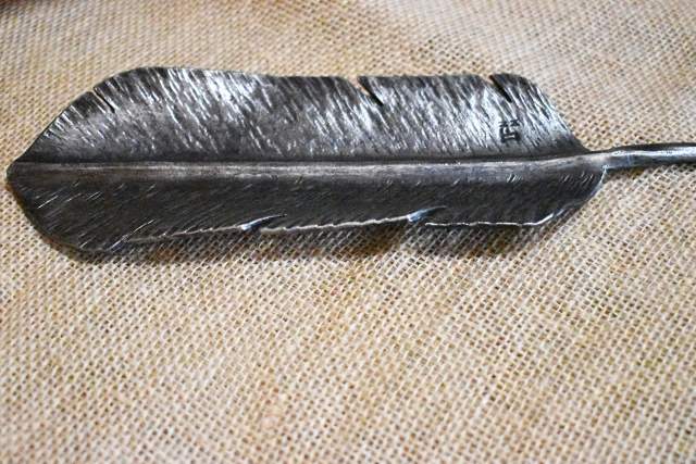 Close-up image of a detailed, steel feather bowl lying on a textured beige surface.