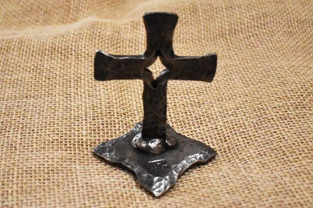A rustic metal cross standing on a burlap fabric background.