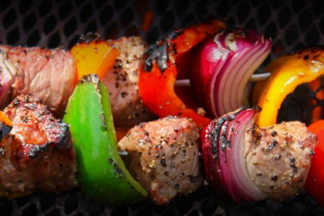 Grilled skewers featuring chunks of steak and mixed vegetables such as bell peppers and onions, on a barbecue grill.