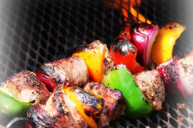 Grilled skewers with chunks of beef and colorful vegetables including red onion, green and yellow bell peppers, charred over an open flame.