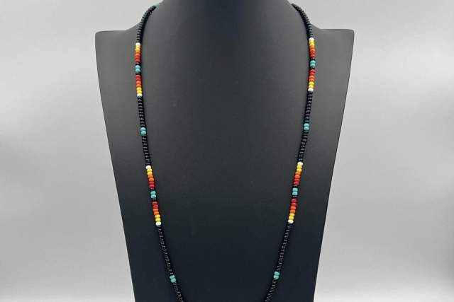 A necklace displayed on a black stand. It features a pattern of different colored beads.