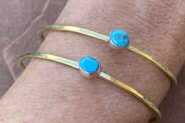 Two turquoise-studded gold bracelets worn on a wrist.