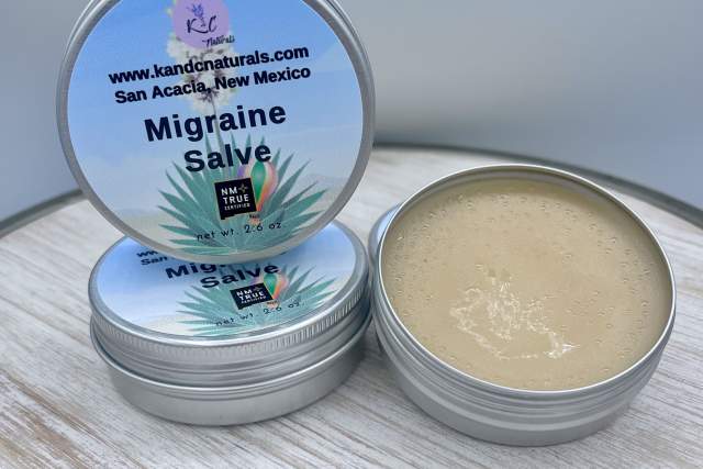 Two tins of K and C Naturals Migraine Salve from San Acacia, New Mexico, one closed and one open displaying the balm inside, placed on a light grey surface.