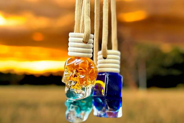 Three colorful glass skull pendants hanging against a vibrant sunset backdrop with a field.