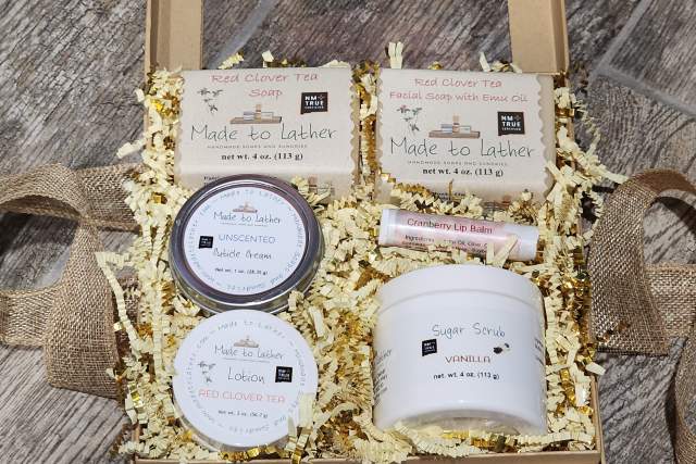 Gift box containing Red Clover Tea skincare products, including soap, lotion, lip balm, and sugar scrub, arranged on shredded paper with a burlap ribbon.