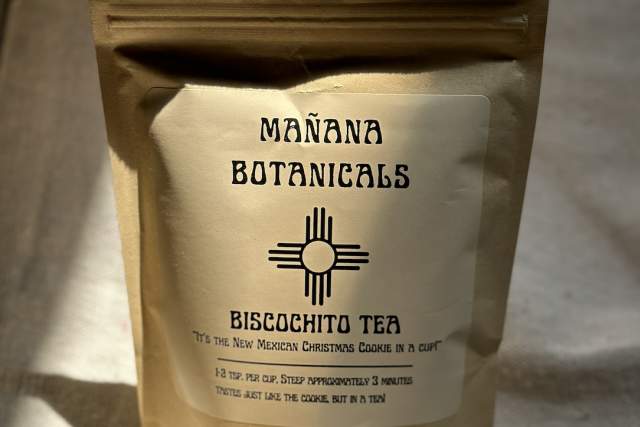 A package of Mañana Botanicals Biscochito Tea, described as "New Mexican Christmas Cookies in a Cup," standing on a table with sunlight casting a shadow.