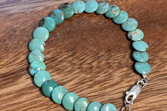 a beaded turquoise necklace with a silver clasp sits on a wooden surface