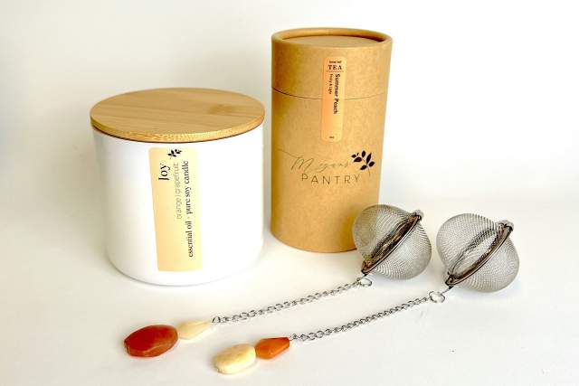 A display featuring two containers labeled "Joy" and "Megan's Pantry" along with a pair of tea infusers with chain handles and amber-colored accents.
