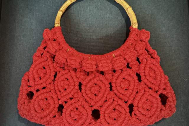 A red handcrafted purse with a bamboo handle, featuring an intricate floral crochet pattern.