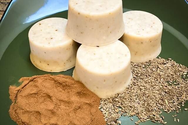 Five round pieces of soap on a green plate, accompanied by piles of ground cinnamon and fennel seeds.