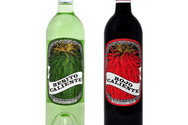 Two bottles of wine, one labeled "Besito Caliente" in a green bottle, and the other labeled "Rojo Caliente" in a red bottle, standing against a white background.
