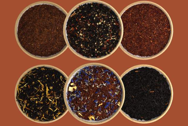 Five bowls of various loose leaf teas displayed against a warm orange background. Each bowl contains a different blend, featuring various colors and textures ranging from dark to vibrant hues.