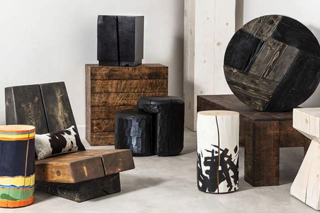 Assorted unique stools and side tables of various shapes, sizes, and designs, including pieces made from different woods and a colorful barrel-shaped stool, displayed against a plain wall.