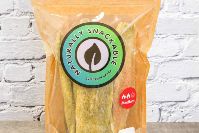 A package of Naturally Snackable dried hatch chiles, marked as medium spice, standing on a table against a brick wall background.