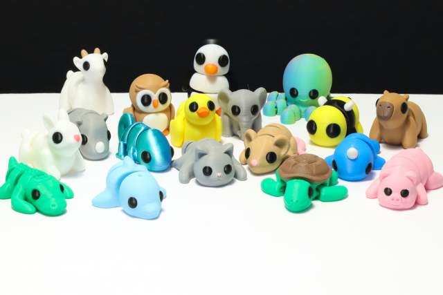 A collection of various colorful animal figurines, including a penguin, rabbits, seals, and others, displayed on a white surface against a black background.