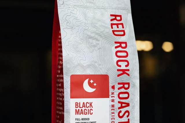 A package of Red Rock Roasters Black Magic coffee, featuring a red and white design with text and logos, set against a dark background.