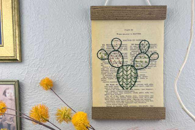 A vintage botanical illustration of various plant species is displayed on a wall, framed by a simple wooden border and hanging by a string.