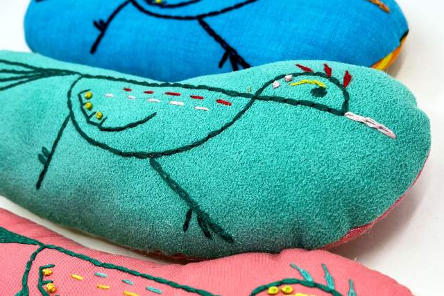Colorful embroidered plushies with bird designs on a white background.