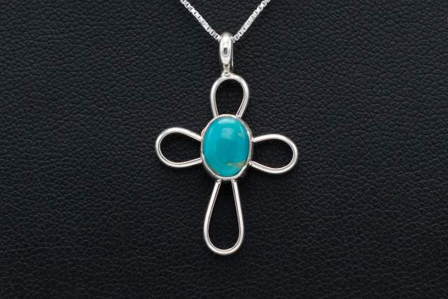 Silver cross pendant with a turquoise center on a chain, displayed against a black textured background.