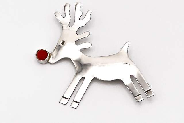 A silver reindeer-shaped brooch with a prominent red nose displayed against a simple, light background.