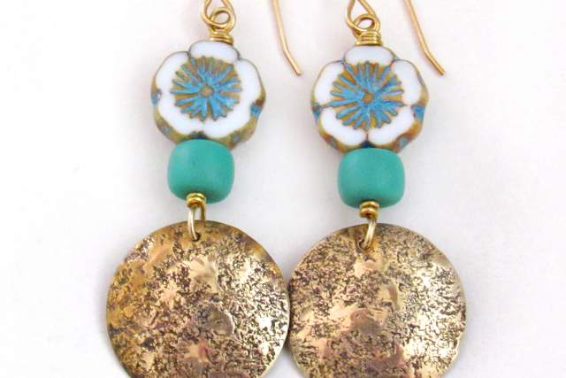 A pair of dangle earrings featuring a flower-shaped bead with blue and white petals, a turquoise bead, and textured gold circular discs hanging below.
