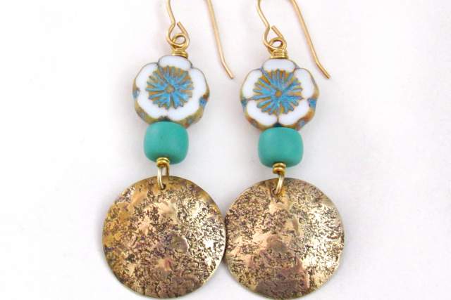 A pair of earrings featuring floral ceramic beads and turquoise stones above textured golden discs.
