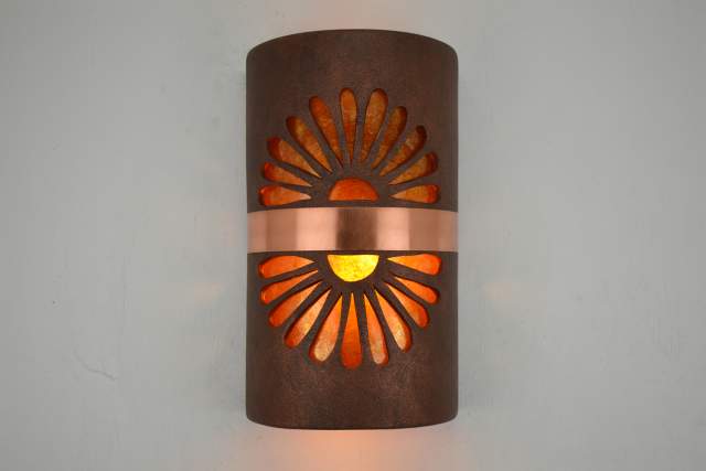 Wall-mounted lamp with a rusted metal exterior featuring a cut-out design of a sunburst, illuminated from within.