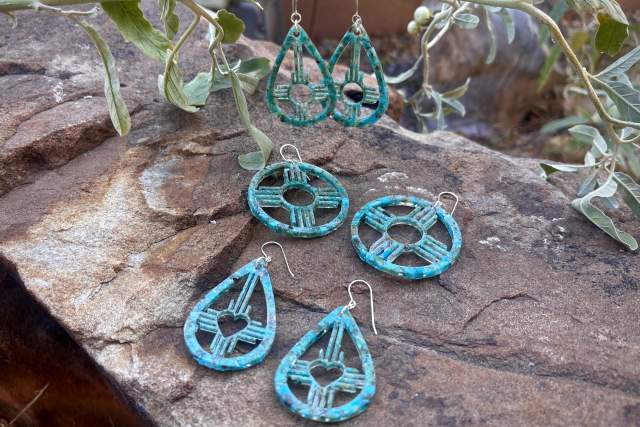 Three pairs of turquoise beaded earrings displayed on a rocky surface with a plant in the background.