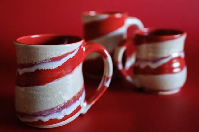 Three ceramic mugs with red and white glaze, arranged in a row against a red background.