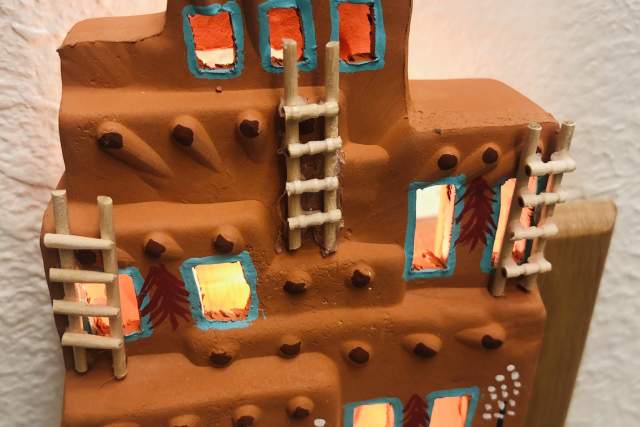A ceramic night light shaped like a Pueblo-style building with small windows and ladder details. It is lit from inside, casting a warm glow