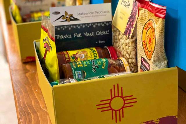 Gift box featuring local products with a "Thanks for Your Order" note and a symbol resembling the New Mexico state flag. Items include coffee, snacks, and jarred goods.