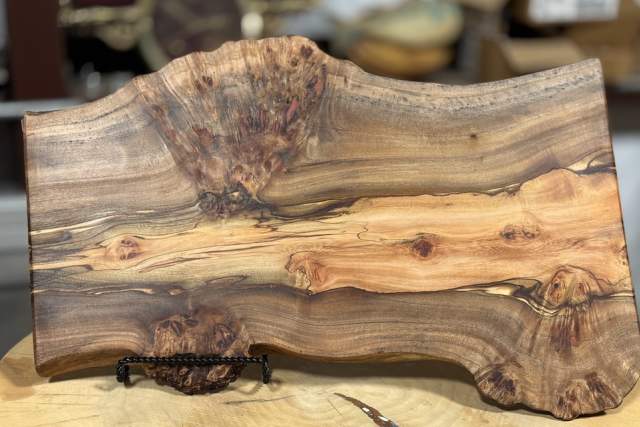 A polished, intricately grained wooden slab displayed on a wooden surface, featuring rich, swirling patterns and natural knots.