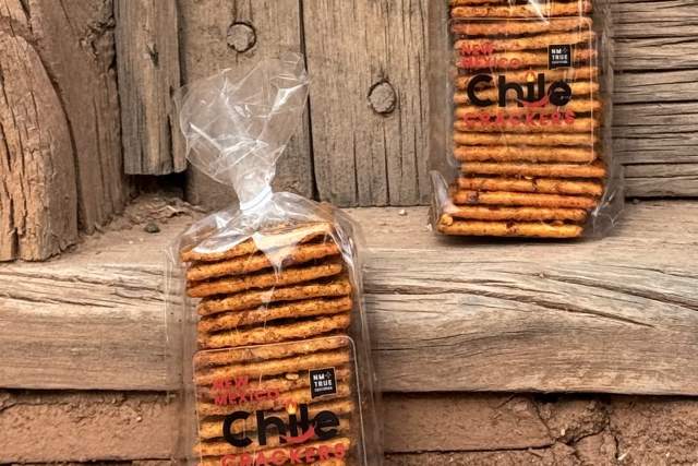 Packages of "Chile Crackers" snacks are placed on rustic wooden steps. The packaging shows stacked crackers in clear plastic bags.