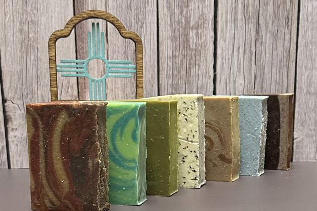 Various colorful bars of soap on a grey surface with Zia symbol against a wooden background