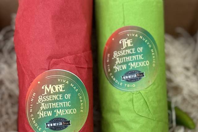 Two bottles of 'Viva Auténtico New Mexico Essence' hot sauce, one wrapped in red paper and the other in green, each adorned with a chili pepper, are presented in a box with straw padding.