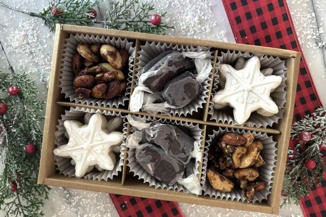 Holiday gift box containing an assortment of treats, presented on a table with a festive red plaid cloth and seasonal decorations.