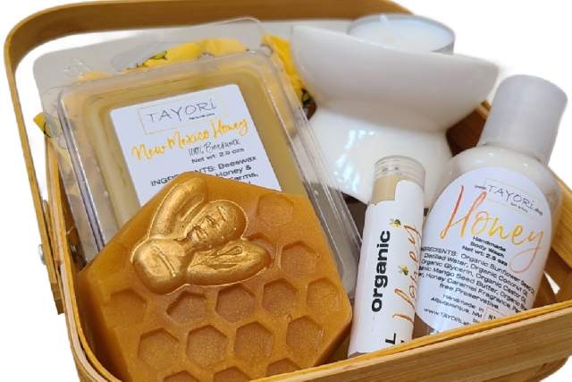 A gift basket containing TAYORI brand beauty products, including honey-themed soap, moisturizing creams, lip balm, and a bath bomb, all arranged neatly in a woven basket.