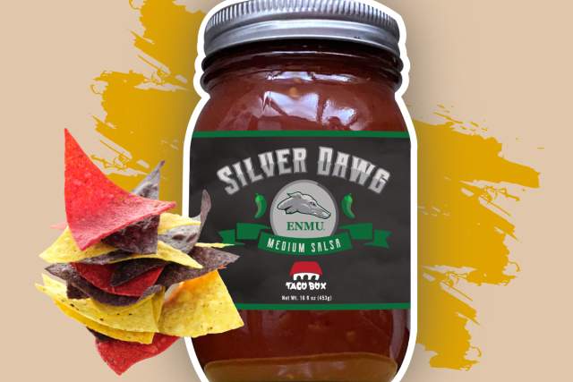 A jar of Silver Dawg medium salsa next to multicolored tortilla chips, set against a background with orange paint splatter.