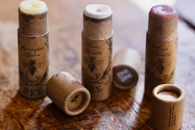 Three cardboard tubes of lip balm are displayed on a wooden surface. The balms are in varying shades. All the tubes are open, showing the lip balm.