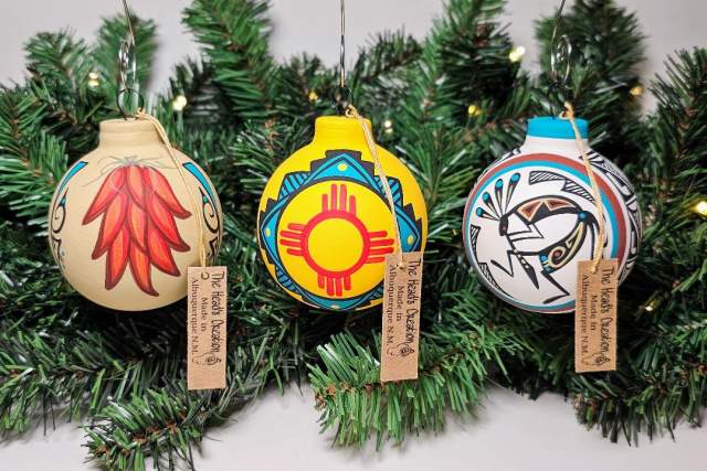 Three colorful ornaments hanging on a pine garland, each featuring unique traditional Indigenous designs.