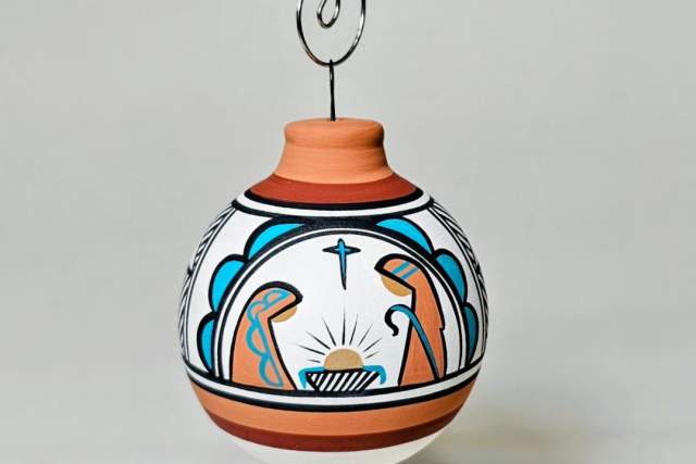 Decorative clay ornament with a Christian nativity scene painted on it, hanging from a metal wire.