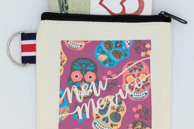 A colorful New Mexico-themed canvas bag with cash and a card sticking out. The design includes vibrant patterns and the state's name prominently displayed.