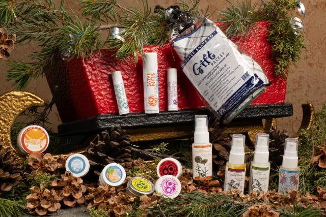 Holiday gift basket featuring a variety of products including lip balms, lotions, and creams, arranged with festive decorations on a textured surface.