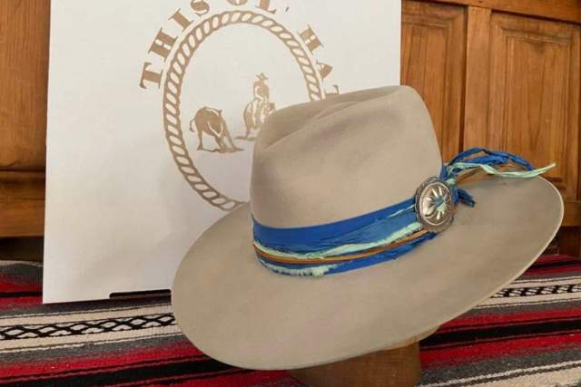 A cowboy hat rests on a patterned fabric with a "This Old Hat" sign featuring a horse and rider in the background.
