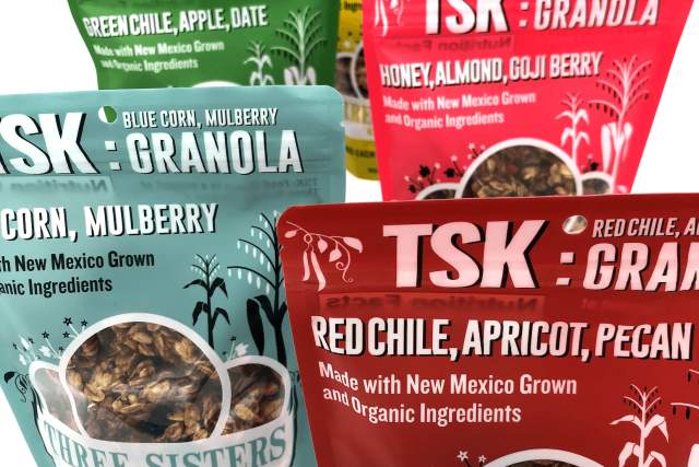 Packages of TSK Granola are displayed, featuring flavors like Blue Corn, Apple Date; Blue Corn, Mulberry; and Honey, Almond, Goji Berry. The colorful packaging includes images of the granola.