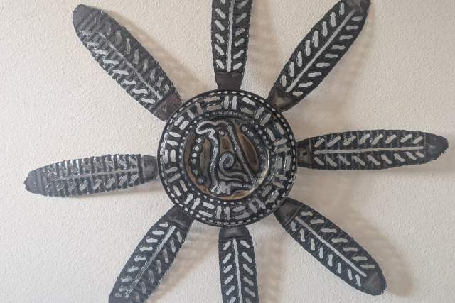 A decorative wall art piece depicting a flower with a bird in the middle with elongated petals, mounted on a white wall.