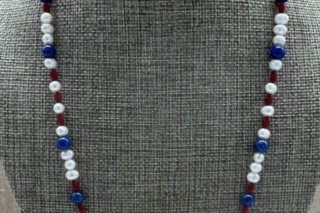 A necklace displayed on a textured stand, featuring white pearls interspersed with multicolored beads.