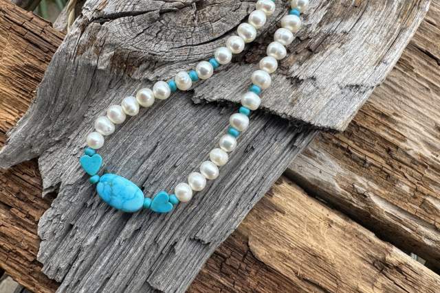 A necklace with pearls and a central turquoise stone laid on a weathered wooden surface.